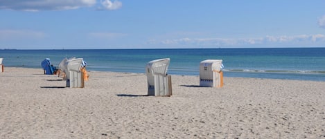 A beach with several wicker beach chairs and a small structure, likely a changing room, on the sand.
