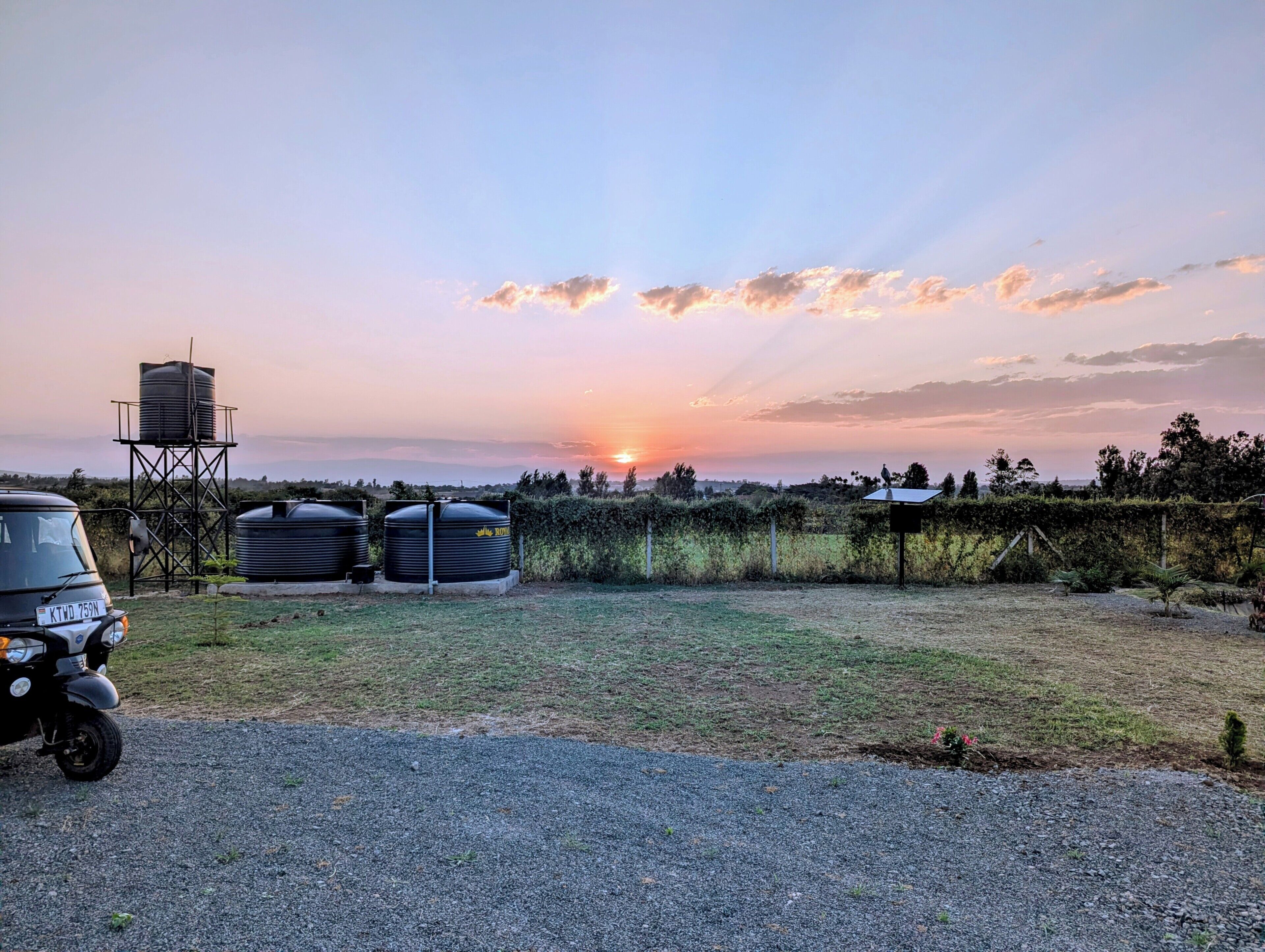 A rural landscape with a sunset, a water tower, and a parked vehicle.