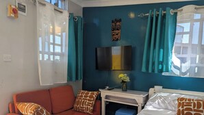 Habitació amb un sofà, un llit, un escriptori amb televisió, una finestra amb cortines i una decoració penjada a la paret.