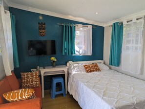 A bedroom with a bed, a desk, a chair, a TV, and a window with curtains.