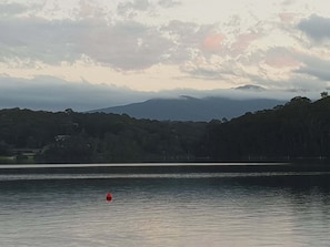 A calm lake with a red buoy in the foreground and a forested hill in the background.