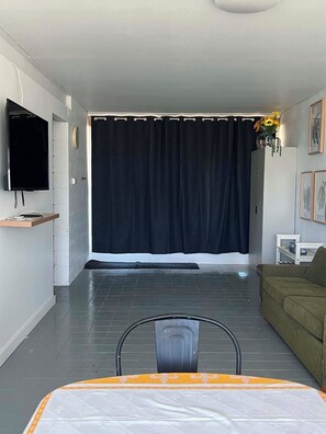 A modern living room with a large window, a flat-screen TV, a sofa, and a dining table.