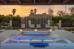 An outdoor pool area with a waterfall feature, seating, and a view of the sunset. - Paradise Reserve | Luxe Pool, GolfSim & Pickleball (Scottsdale)