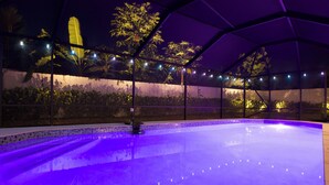 Une piscine intérieure avec un bord carrelé et un éclairage violet.