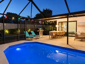 An outdoor pool area with a covered patio, lounge chairs, a dining table, and string lights. - Terra Nova at Delray Beach - Minutes To Beach & Atlantic Avenue (Delray Beach)