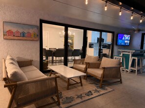 A modern living room with wicker furniture, a flat-screen TV, and a painting of beach houses. - Terra Nova at Delray Beach - Minutes To Beach & Atlantic Avenue (Delray Beach)