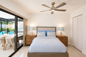 Une chambre avec un lit, deux tables de chevet, un ventilateur de plafond et une vue sur un espace extérieur aménagé avec des sièges.