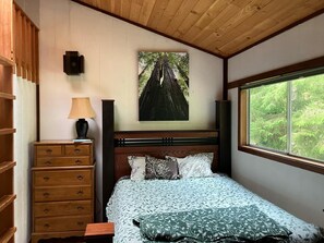 Ein Schlafzimmer mit einem Bett, einer Kommode, einer Lampe, einem Gemälde und einem Fenster.