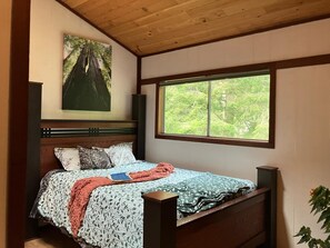 Een slaapkamer met een bed, een raam en een schilderij aan de muur.