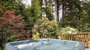 Un jacuzzi rodeado por una terraza de madera y abundante vegetación.