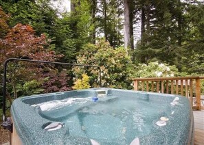 Een hottub omringd door een houten terras en weelderige begroeiing.