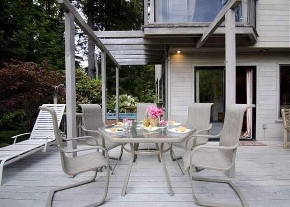 Een terras met tafel en stoelen, een overdekt gedeelte en een huis op de achtergrond.
