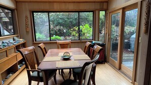 Un comedor con una mesa de madera, sillas y vistas al jardín a través de ventanas amplias.
