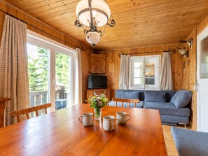 A wooden interior with a dining table, chairs, a sofa, and a television.