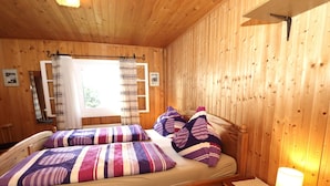 Ett rum med träpanel, en säng, ett nattduksbord och ett fönster med gardiner.