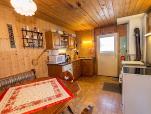 A wooden interior with a dining table, kitchen area, and a door leading outside.