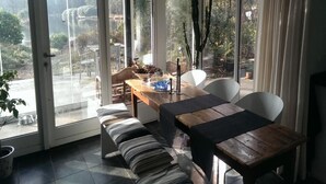 Comedor con banco, mesa y sillas, y vista a árboles y un cuerpo de agua.
