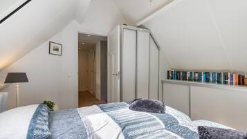 A bedroom with a bed, a bookshelf, and a door leading to another room.