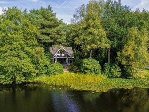 A house surrounded by dense trees and a pond with lily pads. - Beautiful nature house in a wooded area. (Een)