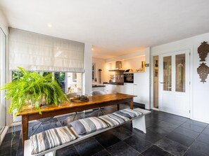 A modern kitchen with a dining area, featuring a wooden table and bench, a large window with blinds, and a view of the outside. - Beautiful nature house in a wooded area. (Een)
