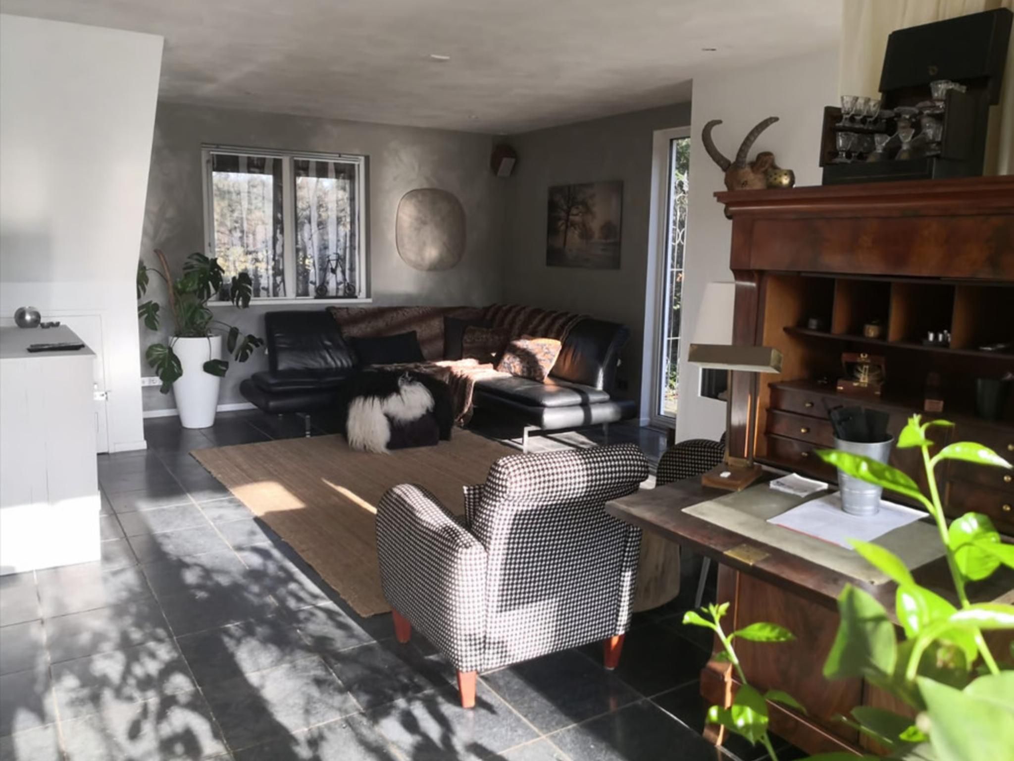 Una sala moderna con un sofá de cuero negro, un sillón estampado y un comedor con una mesa y sillas de madera.