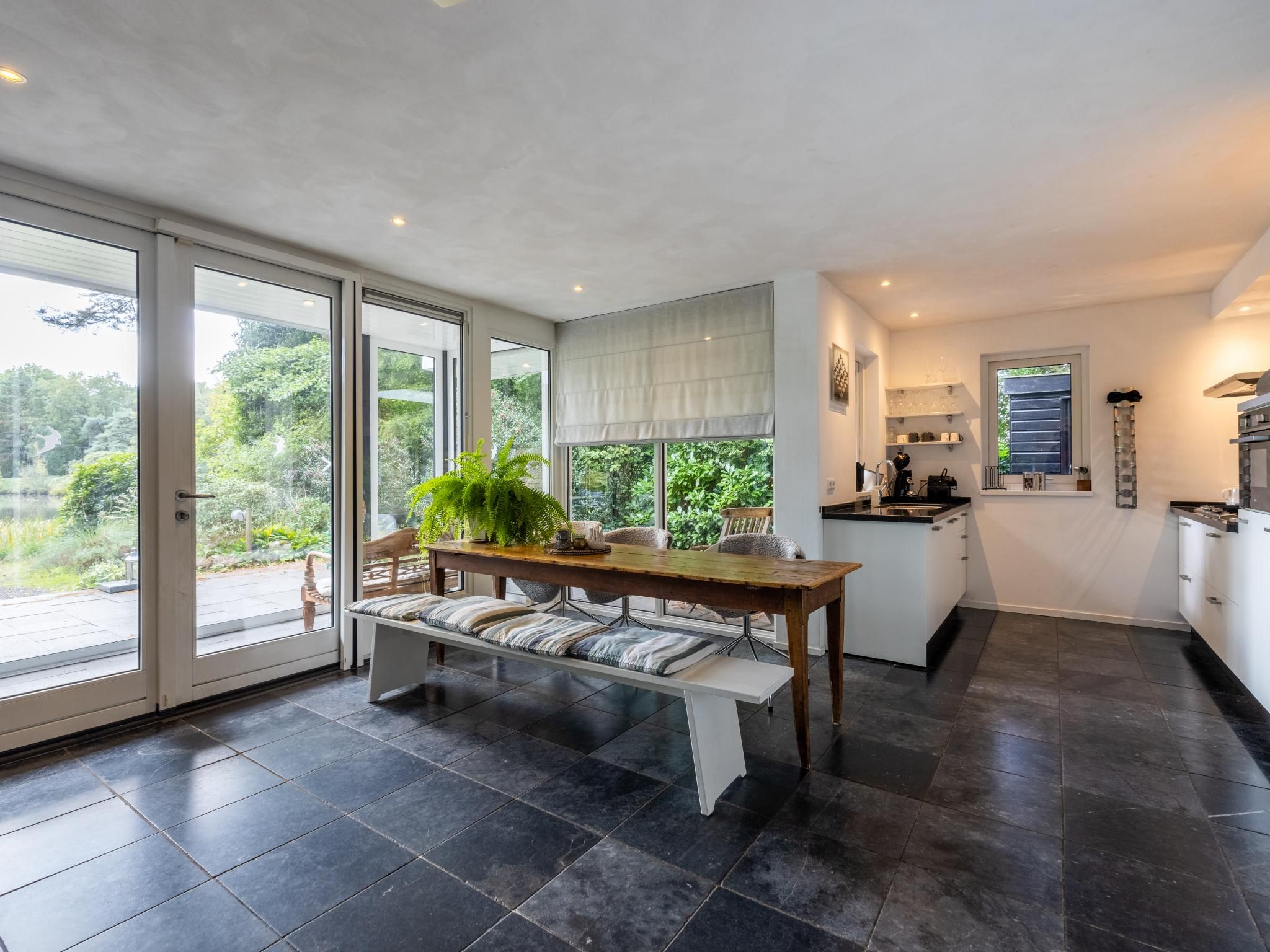 A modern kitchen with a dining area, featuring a large window, a bench, and a potted plant.