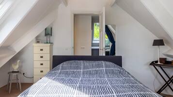 A bedroom with a sloped ceiling, a bed with a patterned bedspread, a dresser, a lamp, and a window.