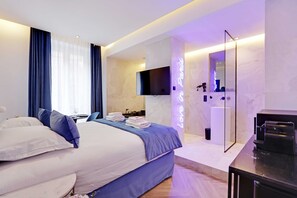 A modern hotel room with a large bed, a flat-screen TV, a mirror, and a bathroom with a shower and toilet. - Suite With AC and Jacuzzi Beaubourg Le Marais (Paris)