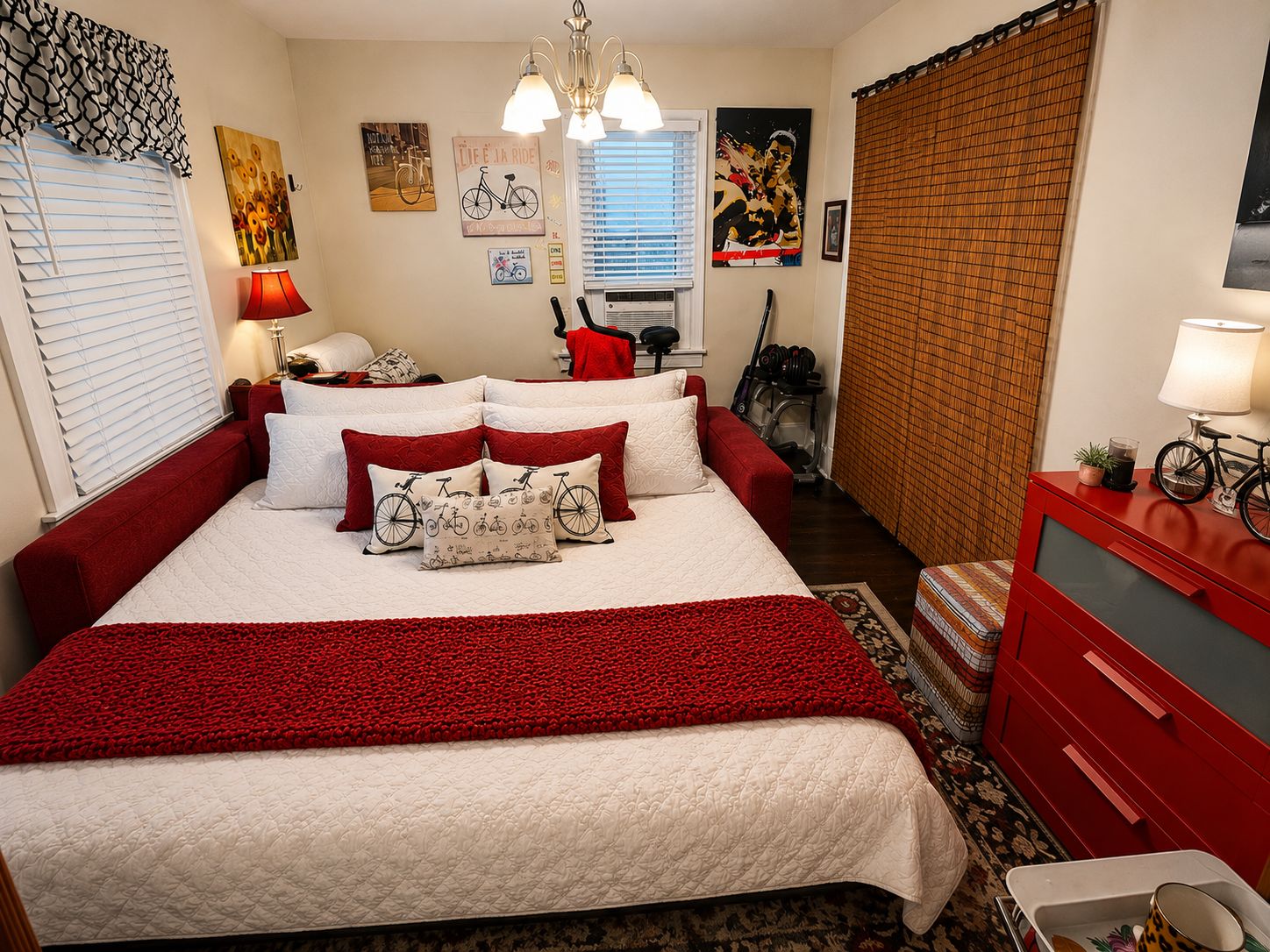 Un dormitorio con una cama grande, un aparador rojo, una bicicleta y diversas obras de arte en la pared.