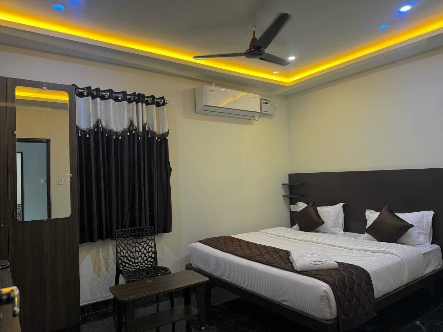 A hotel room with a bed, a chair, a desk, an air conditioning unit, and a ceiling fan.
