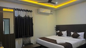 Una habitación de hotel con cama, una silla, escritorio, unidad de aire acondicionado y ventilador de techo.