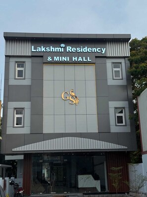 A building with a sign reading 'Lakshmi Residency & Mini Hall' and a logo with a peacock.