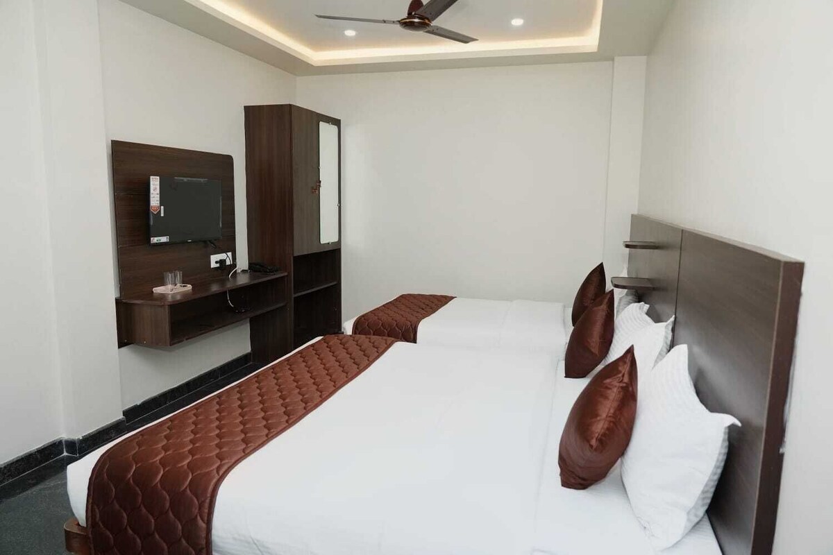 A hotel room with two beds, a TV, a wardrobe, and a ceiling fan.