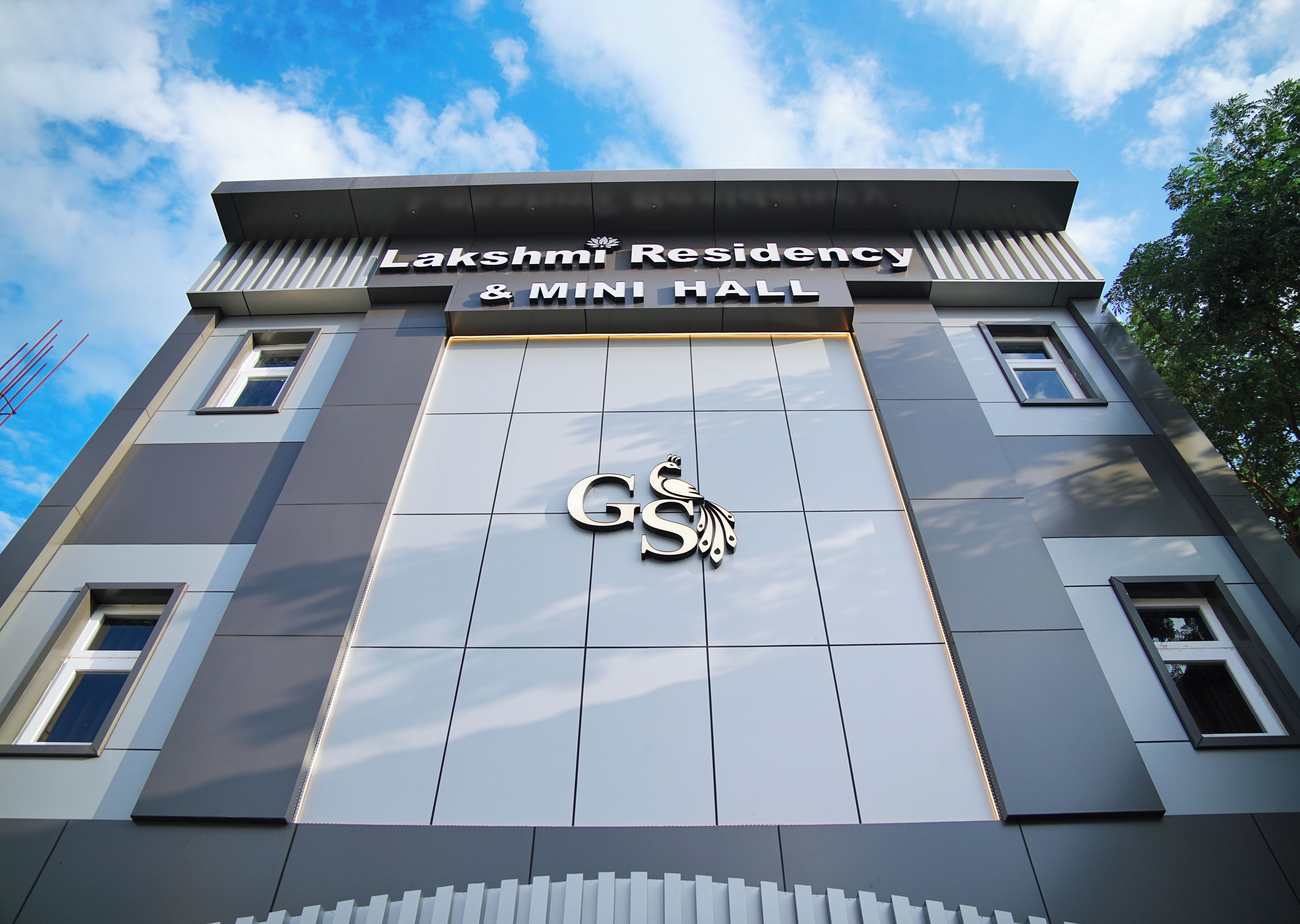 A building with a sign reading 'Lakshmi Residency & Mini Hall' and a logo with 'GS' and a decorative element.