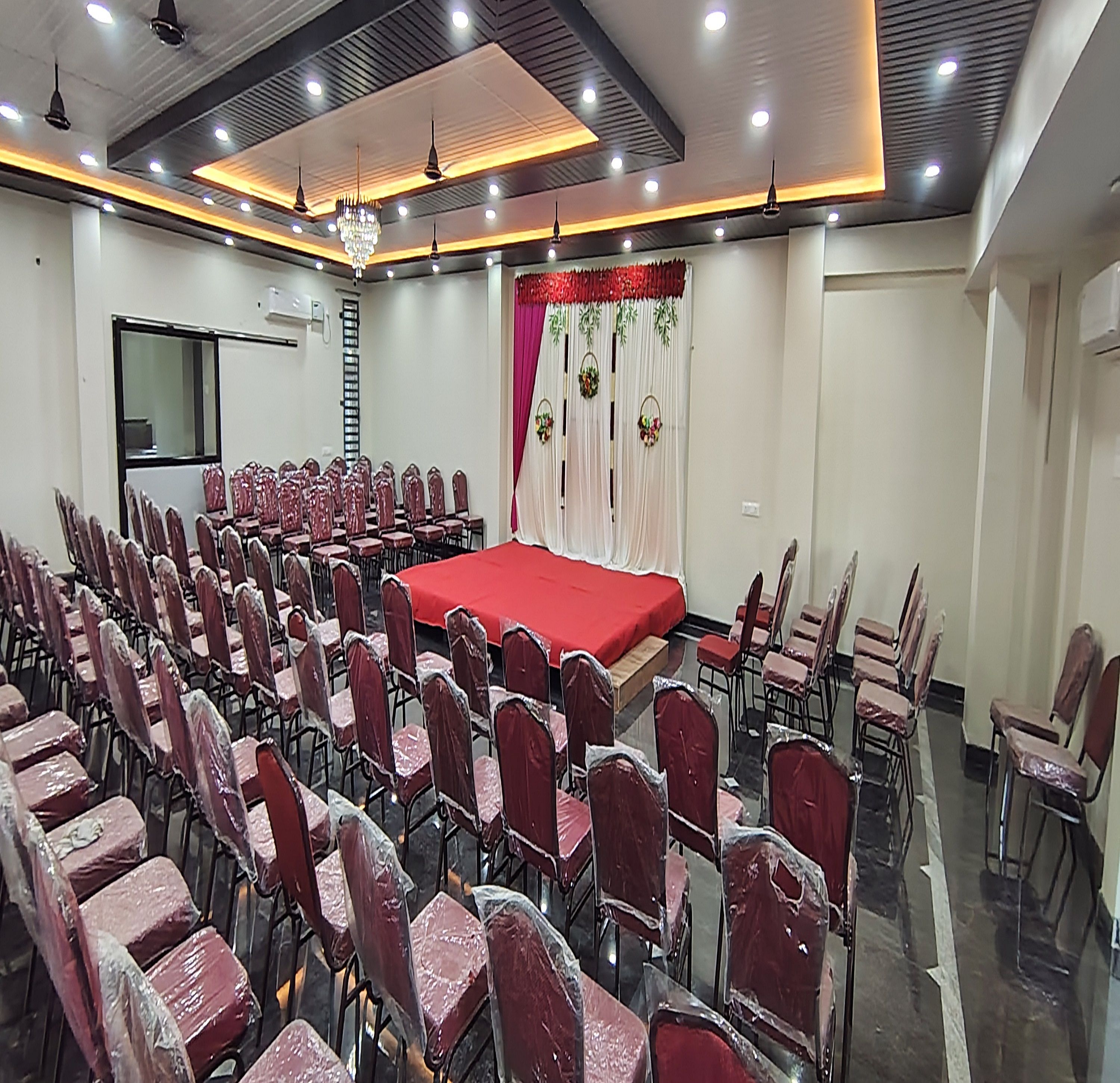 Un salón de conferencias con filas de sillas, un escenario con alfombra roja y una araña de cristal.