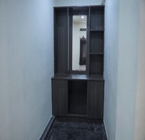 Un pasillo estrecho con un armario de madera oscura adosado a la pared, una ventana pequeña con cortina y un suelo de baldosas.