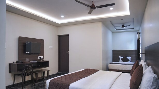 Ein Hotelzimmer mit Bett, Schreibtisch, Stuhl, Fernseher und Deckenventilator.