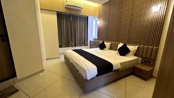 Habitación de hotel moderna con una cama grande, una mesita de noche y un ventanal con cortinas.