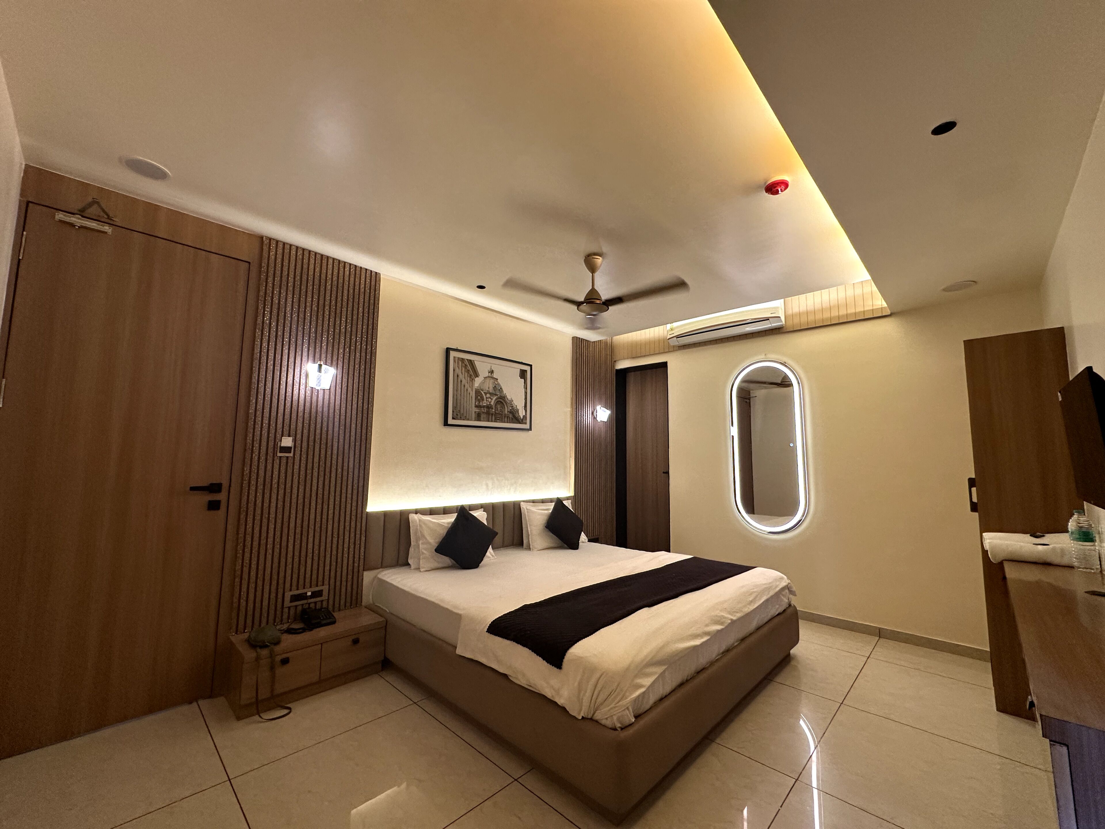 A modern hotel room with a large bed, a wardrobe, a bedside table, a mirror, and a ceiling fan.
