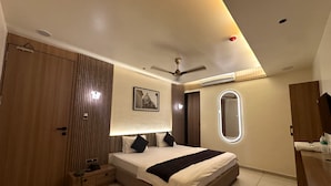 Quarto de hotel moderno com uma cama grande, guarda-roupa, mesa de cabeceira, espelho e ventoinha no teto.