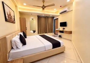 Habitación de hotel con una cama grande, ventilador de techo, unidad de aire acondicionado, televisión y espejo.