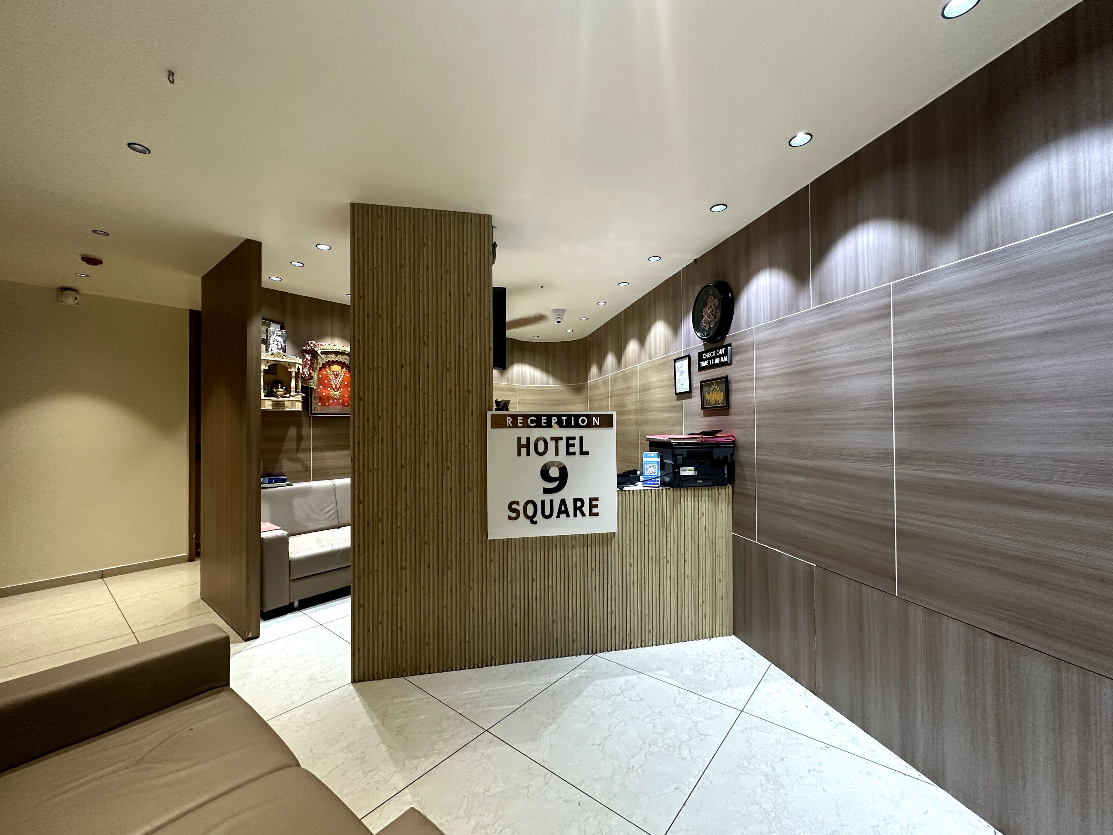 A hotel reception area with a reception desk, a sign indicating the hotel name and room number, and a wall-mounted clock.