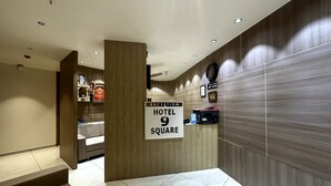 Uma área de recepção de hotel com balcão, placa indicando o nome do hotel e número do quarto, e um relógio fixado na parede.