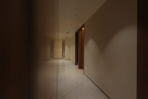 A corridor with a tiled floor and walls, leading to a door with a wooden frame.
