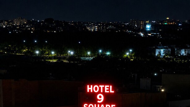 Um edifício com uma placa vermelha chamativa que diz 'HOTEL 9 SQUARE' no topo.
