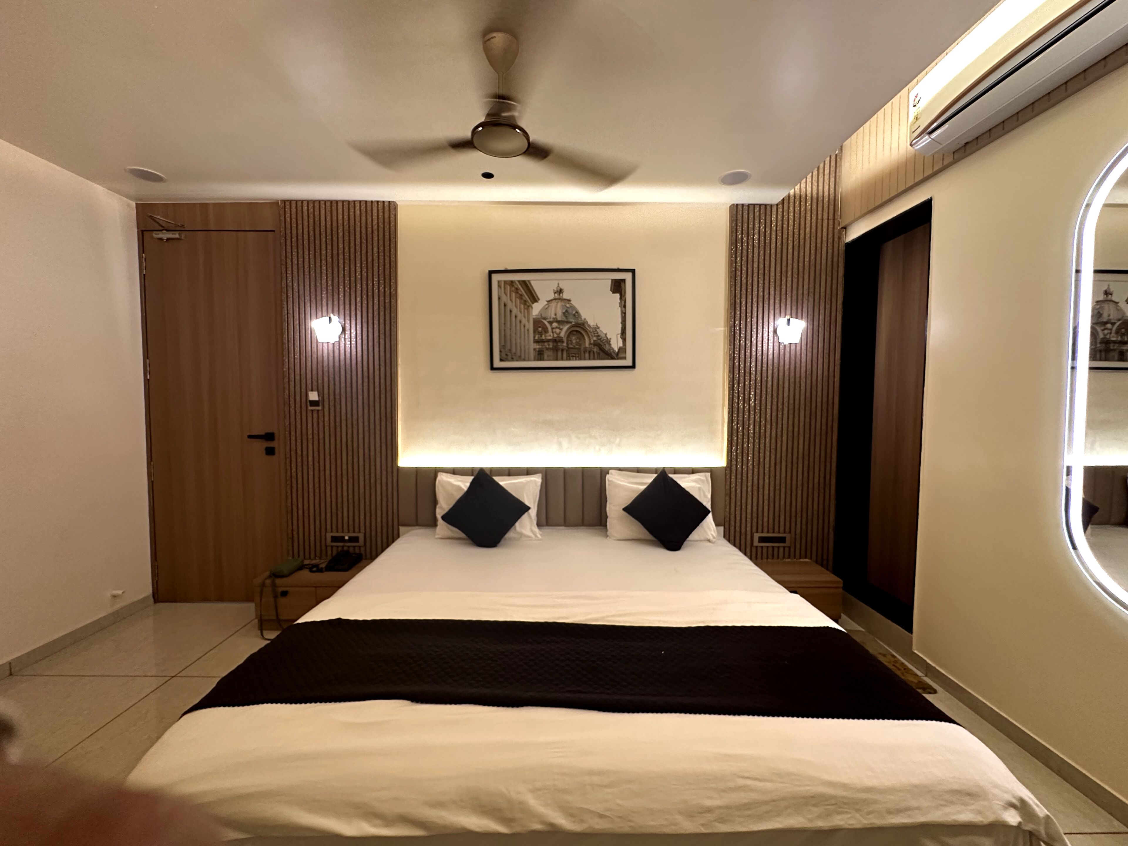 A hotel room with a bed, a ceiling fan, a framed picture on the wall, and a window.