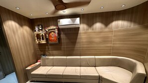 Uma sala de estar moderna com um sofá bege curvo, um ventilador de teto, iluminação embutida e um ar condicionado fixado na parede.