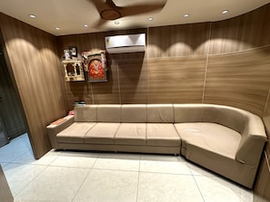 Een moderne woonkamer met een gebogen beige bank, een plafondventilator, inbouwverlichting en een wandairconditioner.
