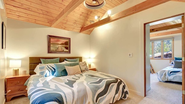 Ein Schlafzimmer mit einem Bett, Nachttischlampen, einem gerahmten Bild an der Wand und Blick durch eine offene Tür.