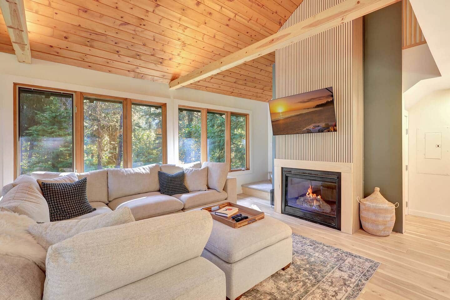 A modern living room with a large sectional sofa, a fireplace, and large windows offering a view of the outdoors.